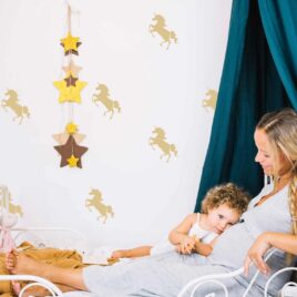 Maman et sa petite fille couchées sur un lit dans une décor féérique de licornes. Des décalques de licornes de couleur beurre sont appliqués sur le mur de la chambre à coucher.
