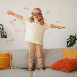 Autocollants muraux avions de papier en origami et petite fille qui saute sur le divan.