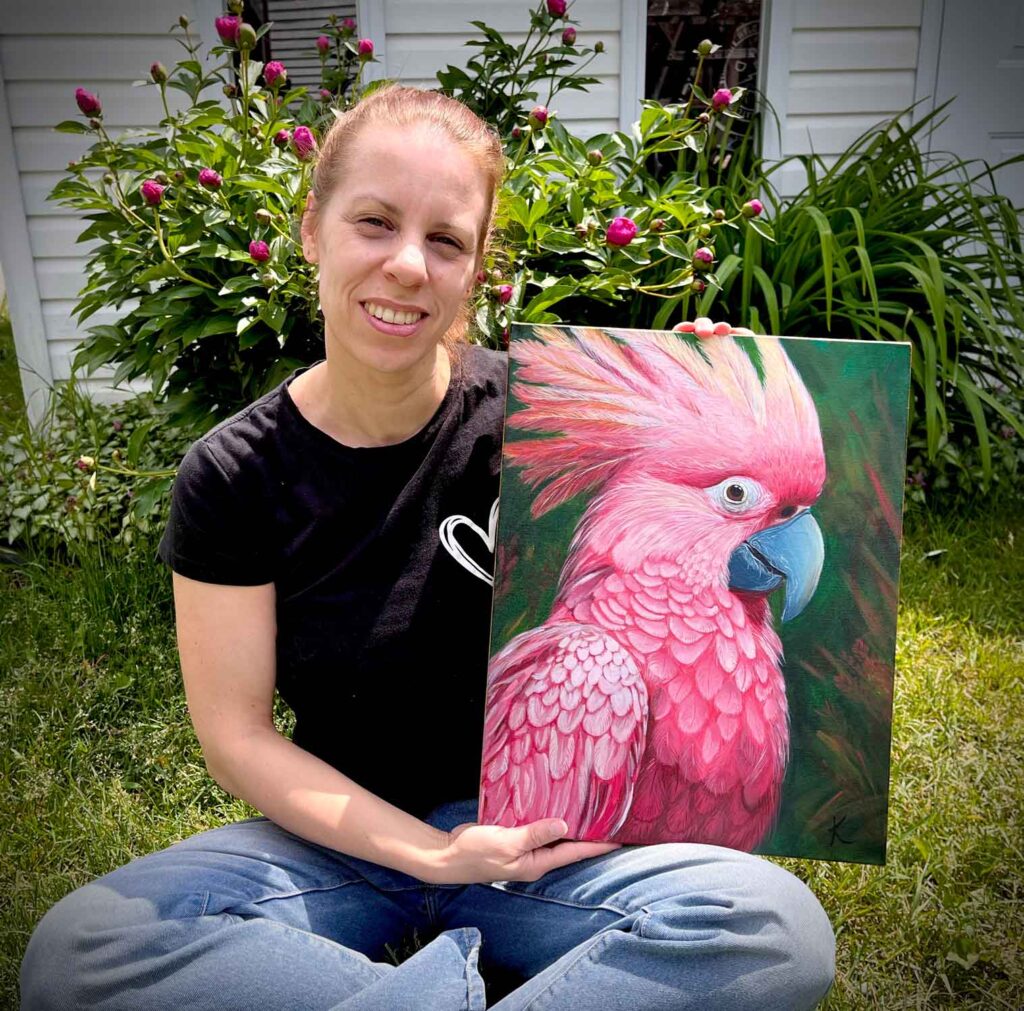 Karine Pothier artiste peintre, tenant fièrement sa toile plumes de rosée, représentant un cacatoès.